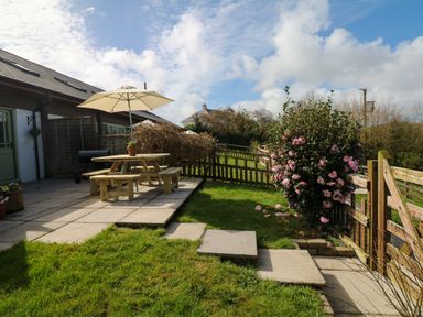 A garden with a wooden picnic table and umbrella on a patio near a flower bush and a wooden fence at Fern Cottage in Muddiford near West Down
