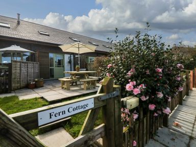 A wooden gate with a Fern Cottage sign leading to a patio with picnic tables and umbrellas at Fern Cottage in Muddiford near West Down
