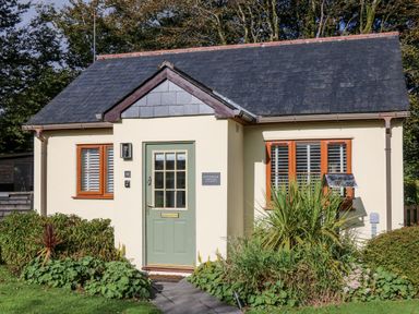 A small cottage with a green door flanked by two windows and surrounded by plants at Inny Brook Cottage in Davidstow near Camelford
