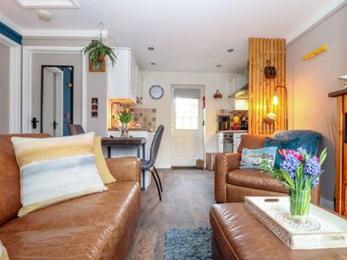A living room with brown leather sofas a vase of flowers on a tray and a kitchen area at Inny Brook Cottage Davidstow near Camelford