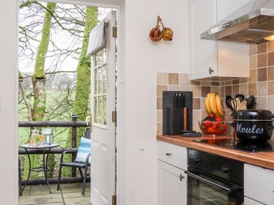 A kitchen with an open door leading to an outdoor seating area with a table and chair at Inny Brook Cottage in Davidstow near Camelford