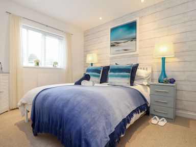 A bedroom with a bed covered with blue blankets and pillows two bedside tables with lamps and slippers on the floor at Inny Brook Cottage in Davidstow near Camelford