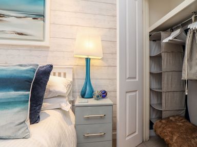 A bedroom with a bed pillow a bedside table with a blue lamp and an open closet with hanging storage at Inny Brook Cottage in Davidstow near Camelford