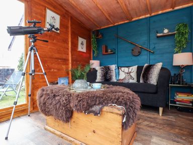 A cozy room with a telescope near a door wooden chest with a furry cover and a sofa with cushions at Inny Brook Cottage in Davidstow near Camelford