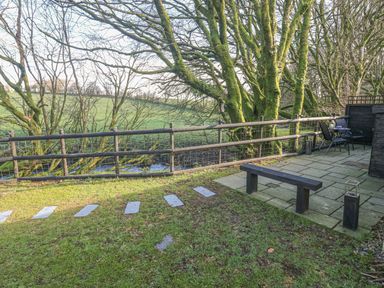 A garden with stepping stones grass bench patio table and chairs near trees at Inny Brook Cottage in Davidstow near Camelford
