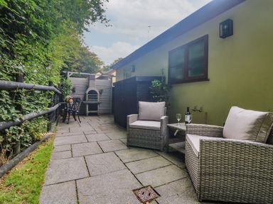 An outdoor patio area with wicker chairs a table a barbecue and greenery at Inny Brook Cottage Davidstow near Camelford