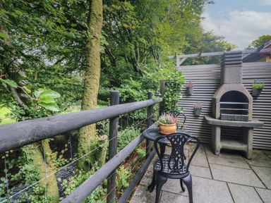 An outdoor patio with a metal table and chairs a barbecue grill and potted plants at Inny Brook Cottage in Davidstow near Camelford