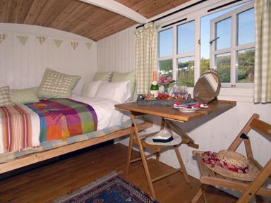 A small bedroom with a single bed a wooden floor a folding table and a chair at Shepherd's Hut in Southerndown near St Brides Major