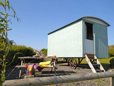 A shepherds hut with a wooden picnic table with blankets and drinks outside at Shepherd's Hut in Southerndown near St Brides Major