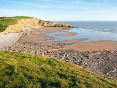 A coastal landscape with a sandy beach rocky shore and grassy cliffs at Shepherds Hut in Southerndown near St Brides Major