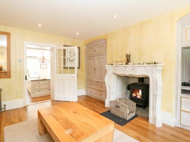 A living room with a wooden coffee table a fireplace with a wood stove an open door leading to a kitchen at The Farmhouse in Felmingham near North Walsham