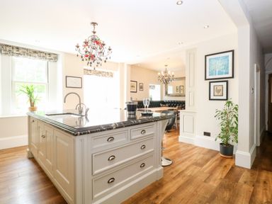 A kitchen island with a sink and drawers in a dining area with chandeliers and framed pictures at The Farmhouse in Felmingham near North Walsham