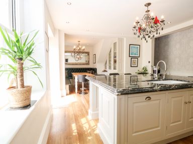 A kitchen with a marble island countertop, sink, black chandelier, dining area with a wooden table, black chairs, and a large mirror at The Farmhouse in Felmingham near North Walsham