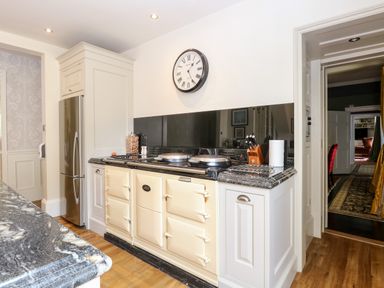 A kitchen with a cream colored stove a stainless steel refrigerator a wall clock and a granite countertop at The Farmhouse in Felmingham near North Walsham