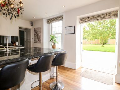 A kitchen with black bar stools and a black countertop near an open door leading to a garden at The Farmhouse in Felmingham near North Walsham