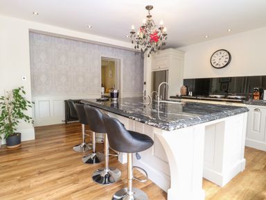 A kitchen with a black marble island counter four black bar stools a chandelier and a wall clock at The Farmhouse in Felmingham near North Walsham