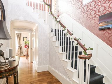 A hallway with a staircase decorated with flowers and a wooden floor at The Farmhouse in Felmingham near North Walsham