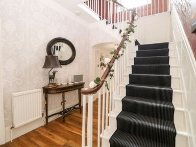 A staircase with striped carpet and floral garland beside a wall with a console table mirror and lamp at The Farmhouse in Felmingham near North Walsham