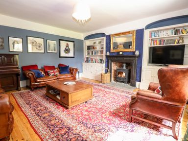 A living room with leather sofas a fireplace a wooden coffee table bookshelves and a piano at The Farmhouse in Felmingham near North Walsham