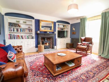 A living room with a leather sofa and armchair a wooden coffee table a fireplace with built in bookshelves and a television at The Farmhouse in Felmingham near North Walsham