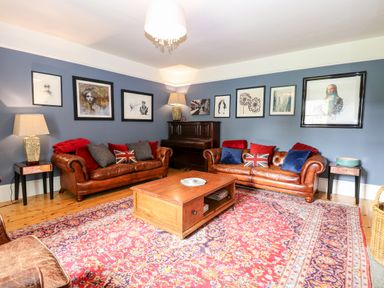 A living room with two leather sofas a wooden coffee table and framed pictures on blue walls at The Farmhouse in Felmingham near North Walsham