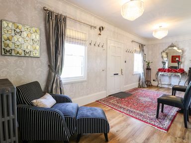 An entrance room with a striped armchair and ottoman a red patterned rug a silver console table with a decorative mirror and red roses at The Farmhouse in Felmingham near North Walsham