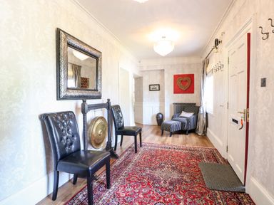 A hallway with two black chairs a gong a large mirror striped armchair red patterned rug and white door at The Farmhouse in Felmingham near North Walsham
