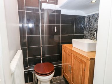 A small bathroom with a toilet with wooden seat and a sink on a wooden cabinet at The Farmhouse in Felmingham near North Walsham