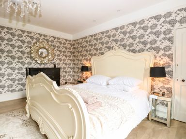 A bedroom with a cream ornate bed two black lamps a black dresser and floral wallpaper at The Farmhouse in Felmingham near North Walsham