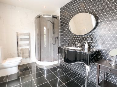 A bathroom with a toilet, corner shower, black patterned wall, black vanity with a round mirror at The Farmhouse in Felmingham near North Walsham