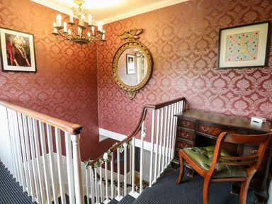 A staircase landing with a wooden desk and chair and patterned wallpaper at The Farmhouse in Felmingham near North Walsham