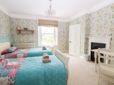 A bedroom with two single beds blue bedspreads floral wallpaper and a fireplace at The Farmhouse in Felmingham near North Walsham