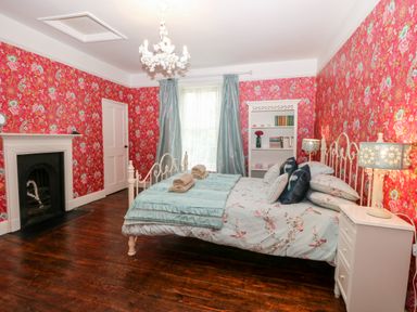 A bedroom with a bed a fireplace a chandelier and floral wallpaper at The Farmhouse in Felmingham near North Walsham