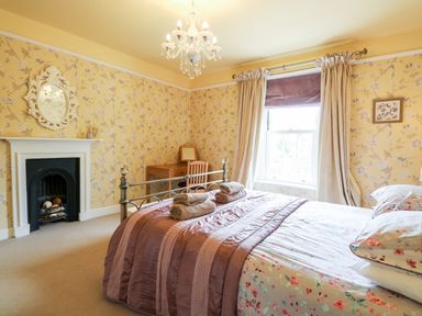 A bedroom with a bed with folded towels on it a fireplace a wooden desk a chair and floral wallpaper at The Farmhouse in Felmingham near North Walsham