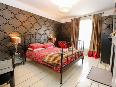 A bedroom with a metal bed frame red bedding bedside tables with lamps a red armchair and gold curtains at The Farmhouse in Felmingham near North Walsham