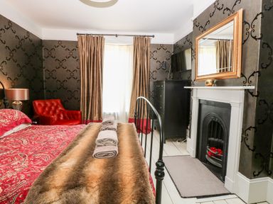 A bedroom with a bed covered with patterned bedding and folded towels with a fireplace mirror armchair and chest of drawers at The Farmhouse in Felmingham near North Walsham