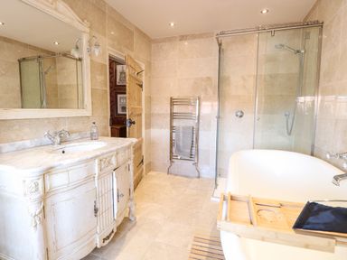 A bathroom with a white vintage vanity unit with marble top a large mirror a glass shower enclosure a white bathtub with a wooden bath tray and a towel rack at The Farmhouse in Felmingham near North Walsham