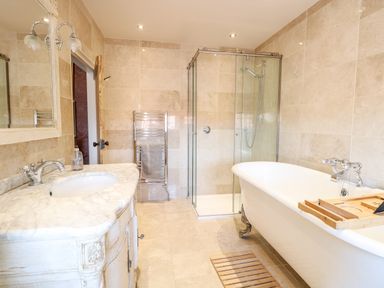 A bathroom with a freestanding bathtub a glass shower a vanity with a marble countertop and a towel rack at The Farmhouse in Felmingham near North Walsham
