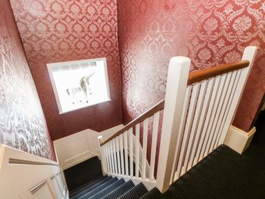 A staircase with white railing red patterned wallpaper and a window with a unicorn figure at The Farmhouse in Felmingham near North Walsham