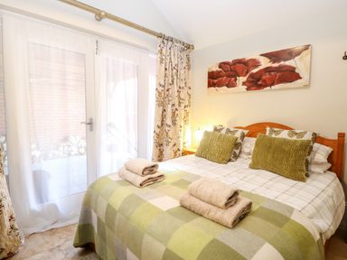 A bedroom with a double bed with pillows and folded towels near glass doors with curtains at The Farmhouse in Felmingham near North Walsham