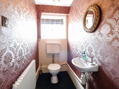 A small bathroom with a toilet a sink a round mirror a radiator and patterned wallpaper at The Farmhouse in Felmingham near North Walsham