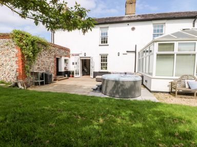 A backyard with a grass lawn wooden deck a hot tub outdoor seating and a white two-story house with a conservatory at The Farmhouse in Felmingham near North Walsham