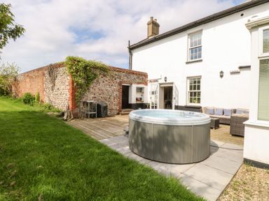 An outdoor patio area with a hot tub a sectional sofa a wooden deck and a brick and flint wall at The Farmhouse in Felmingham near North Walsham