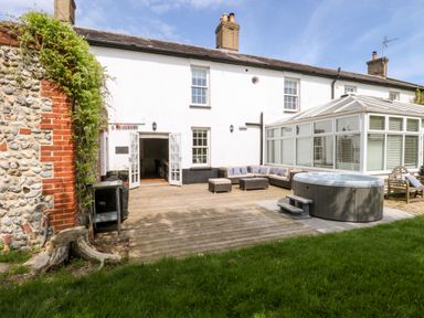 A garden patio with wooden deck seating area hot tub and conservatory at The Farmhouse in Felmingham near North Walsham