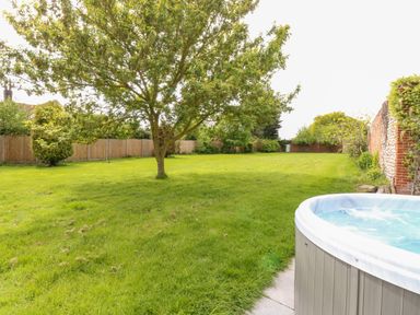A garden with a tree a hot tub green grass and wooden fence at The Farmhouse in Felmingham near North Walsham