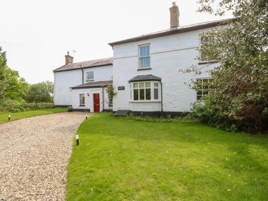 A white farmhouse with a red door gravel driveway and green lawn at The Farmhouse in Felmingham near North Walsham
