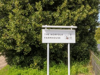 A sign reading The Norfolk Farmhouse with a small illustration of a farmhouse in front of green bushes at The Farmhouse in Felmingham near North Walsham