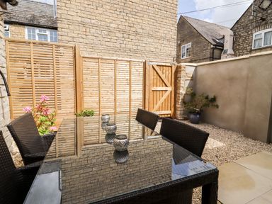 A small outdoor patio with a glass table four wicker chairs wooden fence and potted plants at Mayfield Cottage Nr Malmesbury