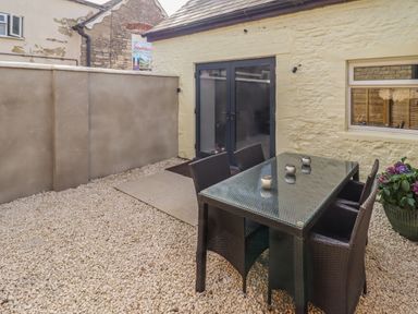 An outdoor patio area with a glass-top table and four chairs on a gravel surface at Mayfield Cottage Nr Malmesbury