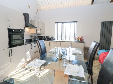 A kitchen with glass dining table set for four and modern appliances at Mayfield Cottage Nr Malmesbury